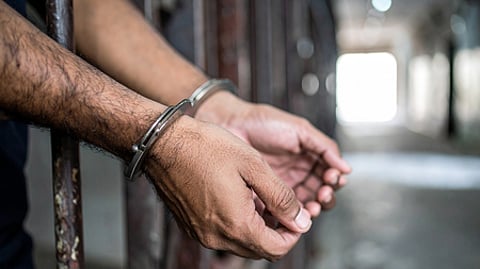 Image of man's hand behind prison bars and his hands are also cuffed
