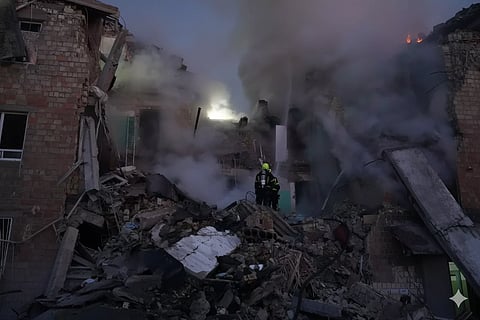 Rescue workers navigate rubble between collapsed buildings as thick smoke rises, conveying the devastation and urgency of an earthquake disaster.