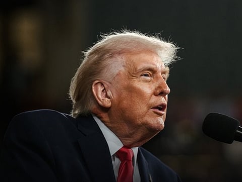 Image of trump speaking in front of a mic. the background is dark and blurred.