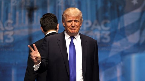 Man in suit with blue tie flashes peace sign, smiling. Another person obscured. Background shows CPAC 2013 logo. Confident, political event.