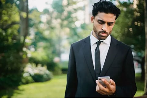 A man in a suit and tie is focused on his smartphone, appearing engaged in a conversation or checking messages.