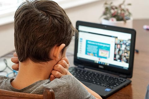 Young school aged boy looking at a laptop computer disinterested in remote learning virtual school class during COVID-19 quarantine.