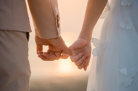 The bride and groom use the little finger together. lovely couple hold hand with sunset background. (Pixabay)