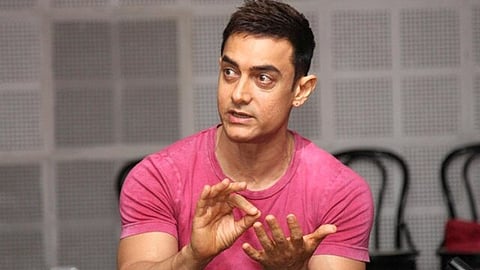 तस्वीर में आमिर खान हाथ के इशारे के साथ कुछ समझाते हुए दिखाई दे रहे हैं।