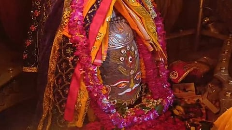 decorated shiva lingam adorned with colourful cloths, garlands of flowers and ornaments inside temple sanctum.