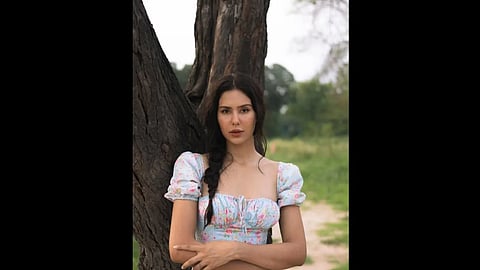 एक लकड़ी के पेड़ के साथ खड़े होकर पोज़ देती नजर आ रही है|