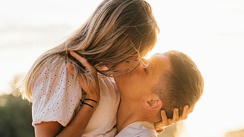 इस तस्वीर में एक लड़का और लड़की किस करते हुए दिख रहे है, और इस में लड़की के बाल भूरे रंग का है और इन दोनों ने सफ़ीद रंग का कपड़ा पहना है