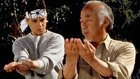 दो लोग कराटे की ट्रेनिंग देते हुए, मिस्टर मियागी की तरह तकनीक सिखाते हुए।