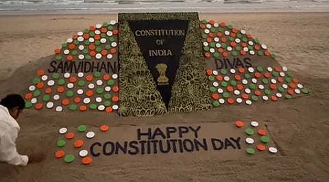 रेत पर 'संविधान दिवस' लिखा हुआ सैंड आर्ट दिखाई दे रहा है|