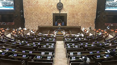 इस तस्वीर में संसद का हॉल दिखाई दे रहा है, जिसमें कई बेंचें और प्रकाश व्यवस्था दिख रही है।