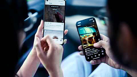 इमेज में दो लोग मोबाइल पर सोशल मीडिया स्क्रोल करते हुए देखे जा सकते हैं।