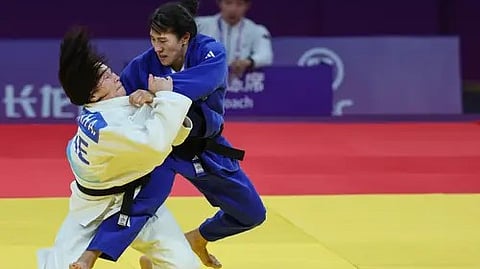 नीले और सफेद परिधान पहने दो लोग ज़मीन पर कुश्ती के मुकाबले में उलझे हुए।