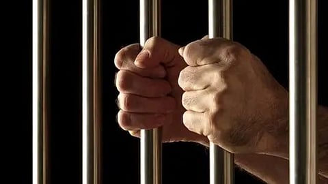 सलाखों के पीछे खड़े व्यक्ति का हाथ|