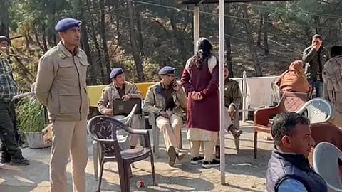 पुलिस अधिकारी खड़े और अन्य लोग बैठे नजर आ रहे हैं|