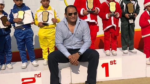 मोहम्मद अजहरुद्दीन बच्चों के साथ पुरस्कार समारोह में मंच पर बैठे हुए, पीछे अलग-अलग रंग की ड्रेस में बच्चे ट्रॉफी पकड़े नजर आ रहे हैं।