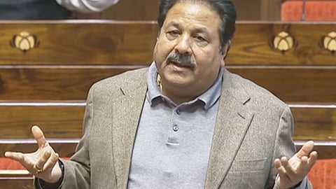 राजीव शुक्ला संसद सदन में खड़े होकर बोलते हुए, ग्रे स्वेटर और ब्राउन ब्लेज़र पहने हाथों से इशारा करते नजर आ रहे हैं।