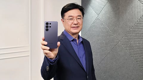 सूट पहने एक व्यक्ति के हाथ में स्मार्टफोन दिख रहा है और वो पोज देता नज़र आ रहा है।