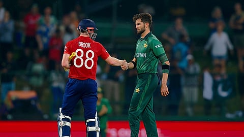 क्रिकेट मैच के बाद इंग्लैंड के बल्लेबाज हैरी ब्रूक और पाकिस्तान के तेज गेंदबाज शाहीन अफरीदी मैदान पर एक-दूसरे से हाथ मिलाते हुए, पीछे दर्शकों की भीड़ दिखाई दे रही है।