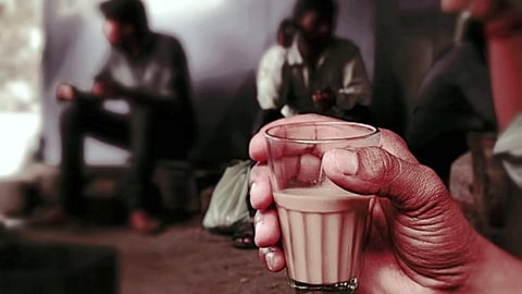 इस चित्र में एक व्यक्ति के हाथ में चाय की गिलास है