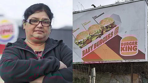 एक महिला काले कपड़ों में हाथ बांधे खड़ी हैं, जबकि साथ में बर्गर किंग का बड़ा विज्ञापन बोर्ड दिखाई दे रहा है, जिस पर बर्गर की तस्वीरें लगी हैं।