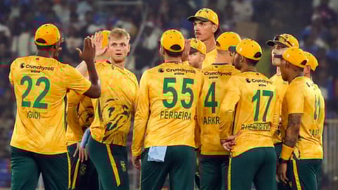 मैदान पर पीले और हरे रंग की जर्सी पहने साउथ अफ्रीका के क्रिकेट खिलाड़ी मैच के दौरान एक साथ खड़े होकर जश्न मनाते हुए दिखाई दे रहे हैं।