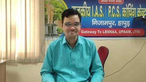 IAS अफसर रिंकू सिंह (IAS Rinku Singh) हरे रंग की शर्ट पहने हुए हैं और पीछे IAS, PCS कोचिंग सेंटर का बोर्ड लगा है।