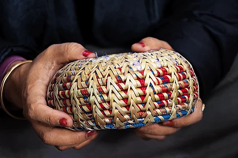 A craftswoman holds a decorative item made of discarded climbing rope interwoven with Moonj, a traditionally harvested wild grass