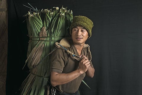 A Lisu man carrying leaves from the forest to help construct a neighbour's house in Nibudi