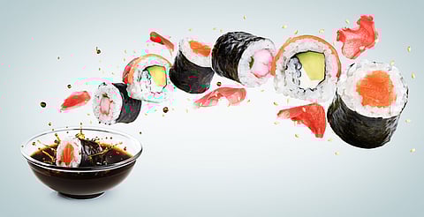 Piece of sushi drops in a bowl with soy sauce.