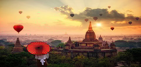 Burmese woman holding traditional red umbrella over the plain of Bagan in misty morning, Mandalay, Myanmar
