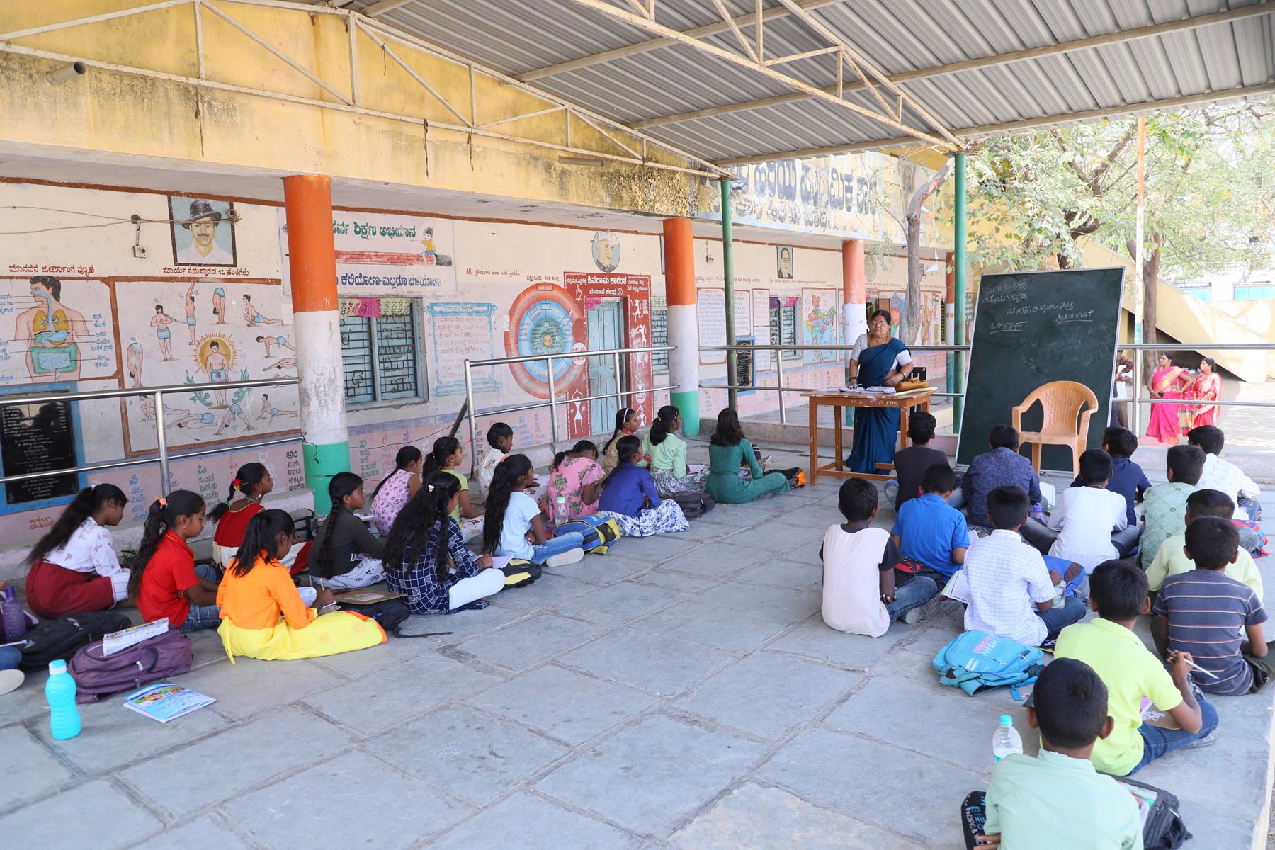 ರಾಯಚೂರಿನ ವಾಲ್ಮೀಕಿ ವೃತ್ತದ ಬಳಿಯ ಕೆಇಬಿ ಕಾಲೊನಿಯಲ್ಲಿರುವ ಹಿರಿಯ ಪ್ರಾಥಮಿಕ ಶಾಲೆಯ ಬಯಲು ರಂಗ ಮಂದಿರದಲ್ಲಿ ಮಕ್ಕಳಿಗೆ ಪಾಠ ಬೋಧನೆ ಮಾಡಲಾಗುತ್ತಿದೆ