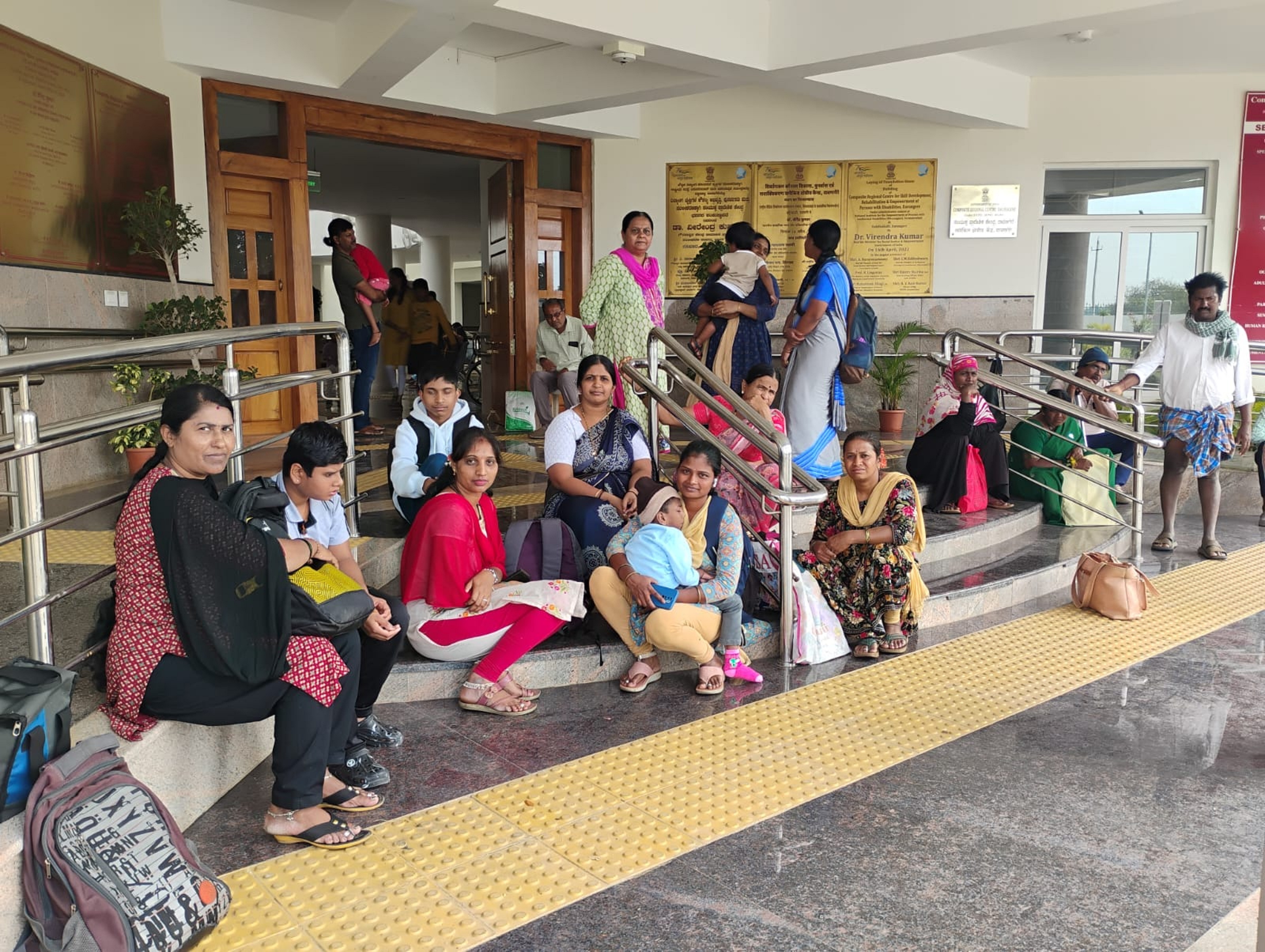 ಸಿಆರ್ಸಿ ಮುಂಭಾಗದ ಮೆಟ್ಟಿಲುಗಳ ಮೇಲೆ ಬಸ್ಗಾಗಿ ಕಾದು ಕುಳಿತಿದ್ದ ಅಂಗವಿಕಲರು ಹಾಗೂ ಪೋಷಕರು