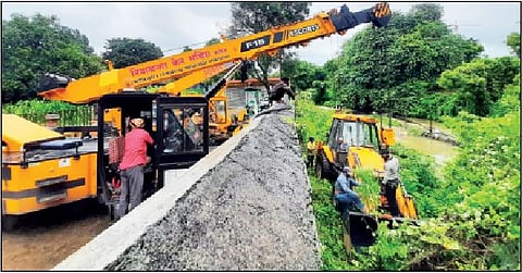 केबलची दुरुस्ती करण्यासाठी दोन क्रेनच्या साहाय्याने जेसीबी ओढ्यात उतरवताना कर्मचारी.