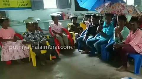 குடை பிடித்துக்கொண்டு பாடம் படிக்கும் மழலைகள்