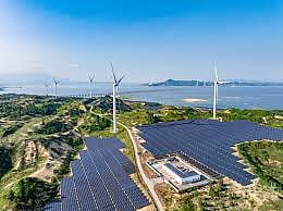 Solar panels and wind turbines installed across a coastal renewable energy site under a clear blue sky.