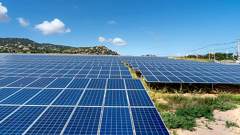Rows of solar panels installed across a large utility-scale solar power plant under a clear blue sky.