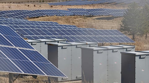 Battery energy storage containers installed alongside solar panels at a renewable energy facility.