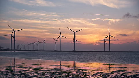 Multiple offshore wind turbines standing in coastal waters during sunset along Germany’s shoreline.