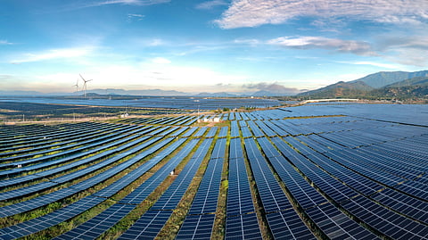 Aerial view of a massive solar farm with wind turbines operating across a mountainous renewable energy landscape.