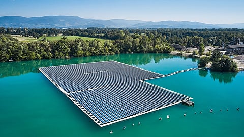 Large floating solar photovoltaic plant installed on a reservoir surrounded by green landscape.
