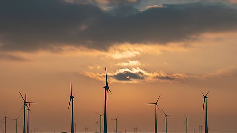 Wind turbines operating at an onshore wind farm under a cloudy sunset sky.