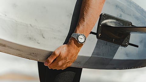 Wrist wearing Bremont SM500 watch holding surfboard at the beach