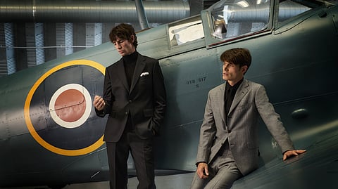 Two men in tailored suits pose beside vintage RAF aircraft in hangar