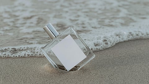 Perfume bottle resting on sandy beach with ocean waves