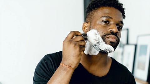 Man shaving at mirror with foam on face