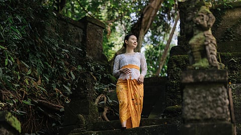 Woman in traditional Balinese attire walking down stone steps in greenery