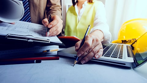 Professionals planning exhibition stand design with laptop and blueprints