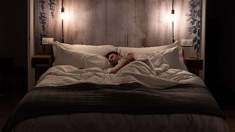 Man sleeping peacefully in a cozy, well-lit bedroom with layered bedding