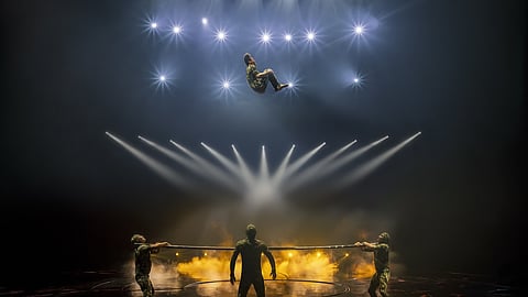 Acrobats perform Russian Bar act with triple somersault under stage lights