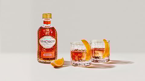 Bottle of Via Carota Classic Negroni with cocktails in Simon Pearce glasses